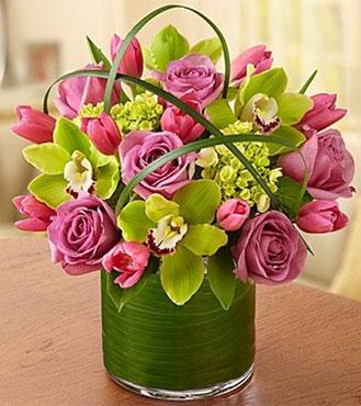 تنسيق زهور نابض بالحياة في مزهرية زجاجية ملفوفة بأوراق خضراء.